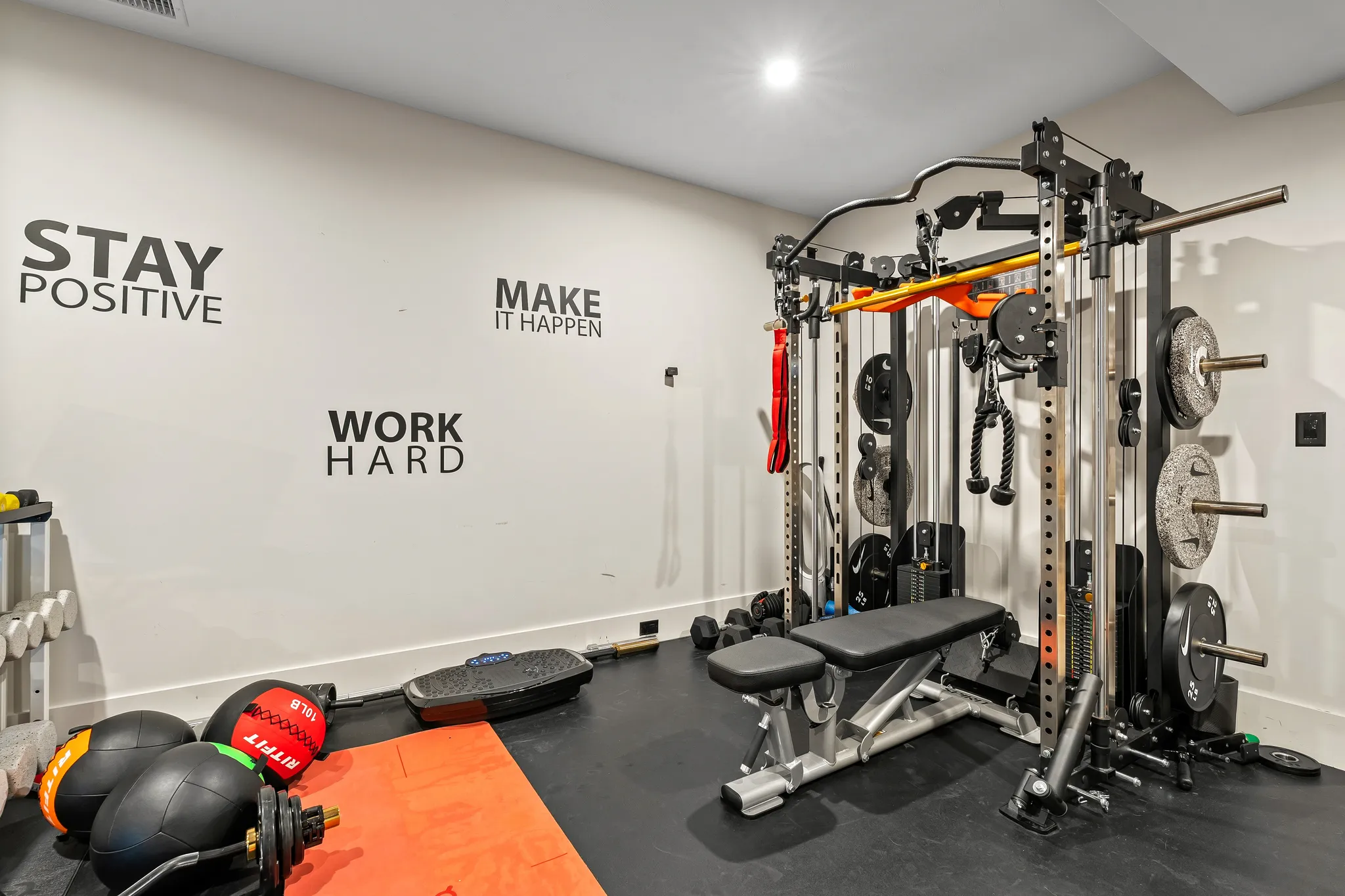A home gym with a multi-functional weight rack, a weight bench, and various exercise equipment, featuring motivational wall decals.