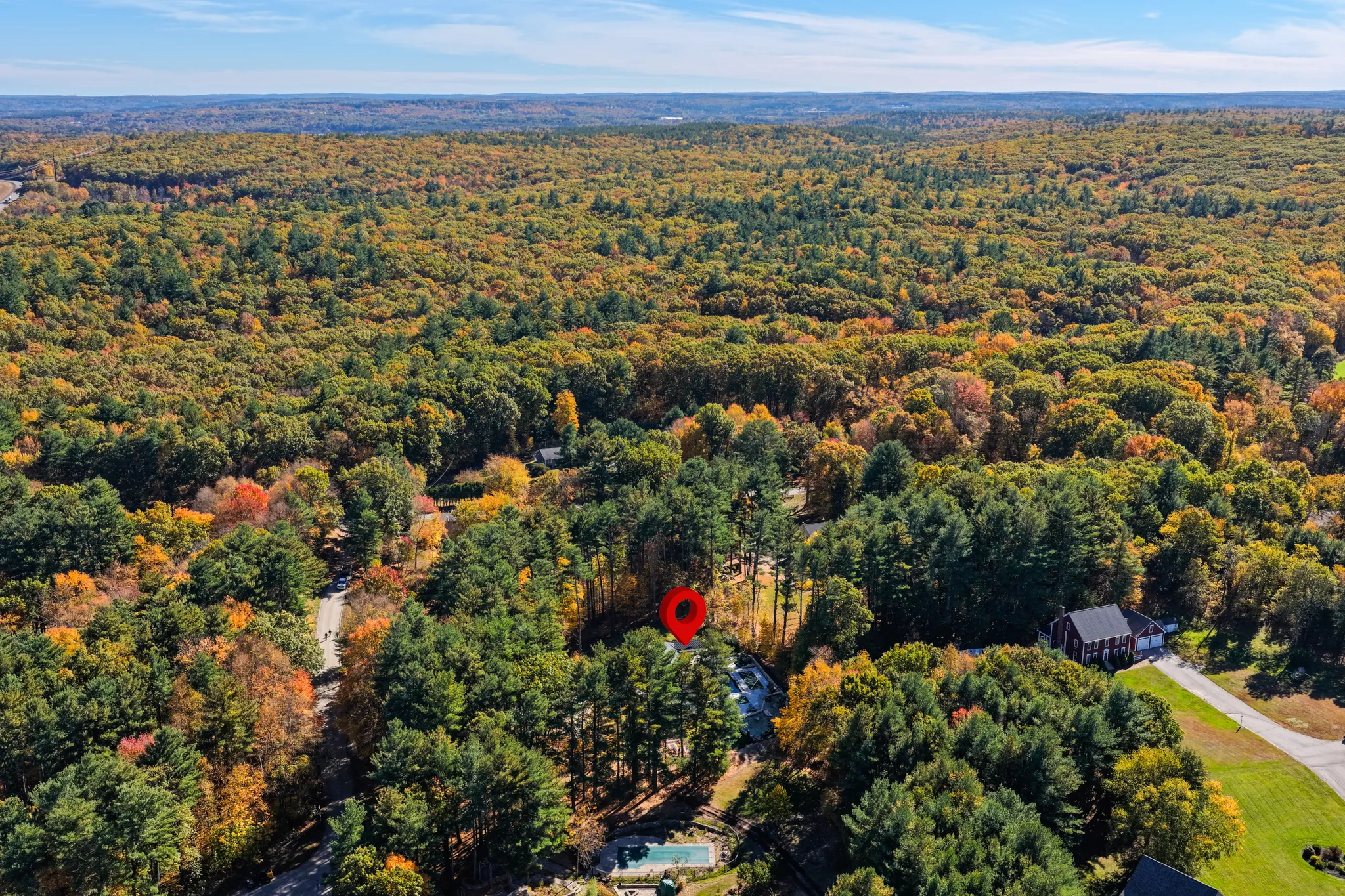 An aerial wide shot shows a residential area surrounded by autumn trees with a swimming pool visible in the foreground.