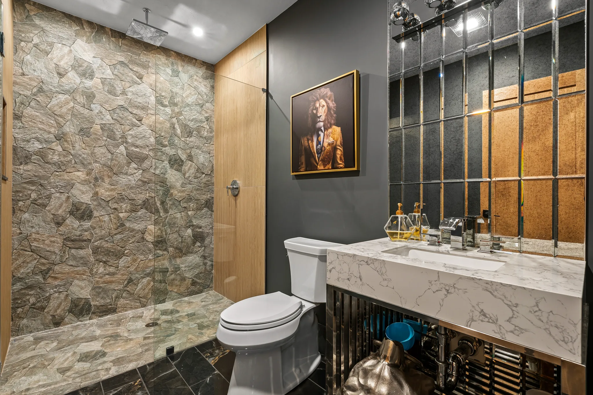 A modern bathroom features a walk-in shower with stone walls, a vanity with a marble countertop, and a decorative mirrored wall.