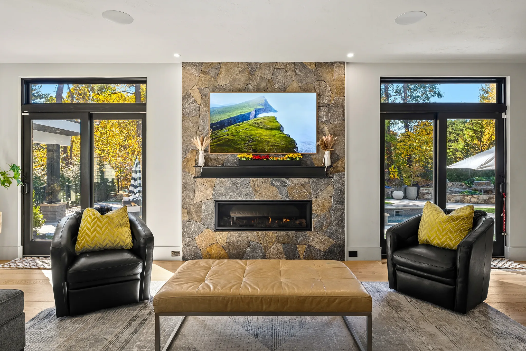 A bright living room with a stone fireplace, television, two armchairs, and an ottoman, featuring large sliding doors to an outdoor view.